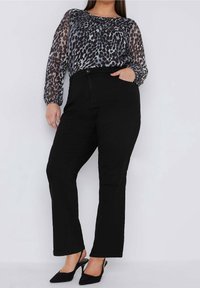 Černé džínsy s vysokým pasem doplněné průhlednou blůzou se vzorem ve šedé a černé barvě s motivem zvířat. Celý outfit dotváří uzavřené lodičky.