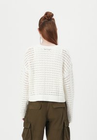 White knitted sweater with a loose fit, featuring a textured pattern, ribbed hem, and long sleeves. Paired with olive green cargo pants.