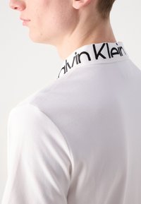 Witte polo met een geribde kraag en een zwart "Calvin Klein" logo. De zachte textuur en de getailleerde pasvorm verbeteren het uiterlijk.