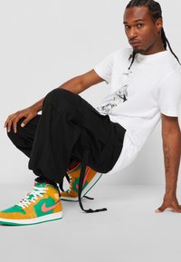 Zapatillas deportivas altas en verde, naranja y rosa, con materiales de ante y cuero; pantalones cargo negros; camiseta gráfica blanca.