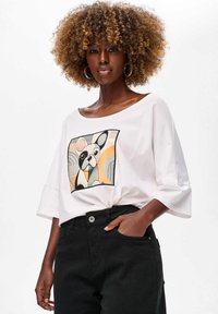 Biała, oversize t-shirt z graficznym nadrukiem psa w kolorach szarości, czerni i pomarańczy. Posiada szerokie rękawy i miękką teksturę.