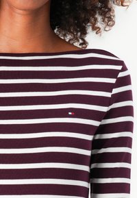 Gestreiftes Langarmshirt aus bordeauxroter und weißer Baumwolle, mit einem Bootsausschnitt und einem kleinen Logo-Patch in Rot, Weiß und Blau auf der Brust.