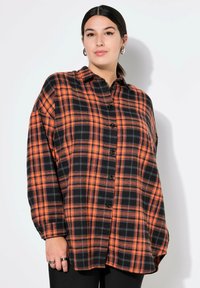 Camicia in flanella nera e arancione con motivo a quadri, davanti con bottoni, maniche lunghe, vestibilità comoda e bottoni neri a contrasto.