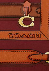 Coach logo ontwerp met een diep rode achtergrond, een bruine en oranje gestreepte patroon, gouden hardware accenten en uitgesproken stikdetails.