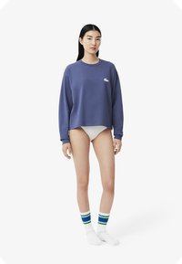 Maglione lungo viola con maniche a giro e logo bianco, abbinato a slip bianchi e calzini a strisce multicolori. Tessuto in cotone liscio.