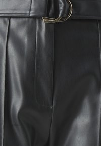 Crne hlače od umjetne kože s nabranim detaljima, elegantnom teksturom i akcentom od metalne zlatne kopče. Glatka i mekana površina sa krojem prilagođenim tijelu.
