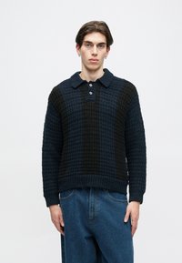 Sötétkék és fekete kötött pulóver, gallérral és három gombos gombolással, texturált mintával és bordás mandzsettákkal.