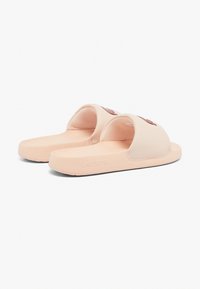 Sandales de奴 en caoutchouc rose avec des brides larges, présentant un design texturé sur le devant et une semelle plate. Logo embossé sur le côté.