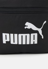 Borsa in tessuto nera con logo PUMA bianco e silhouette di un puma in movimento. Il design include una zip superiore per la chiusura.