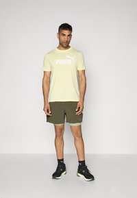 Light yellow t-shirt with white "PUMA" logo, paired with olive green shorts and black athletic shoes with green accents. Minimal design.