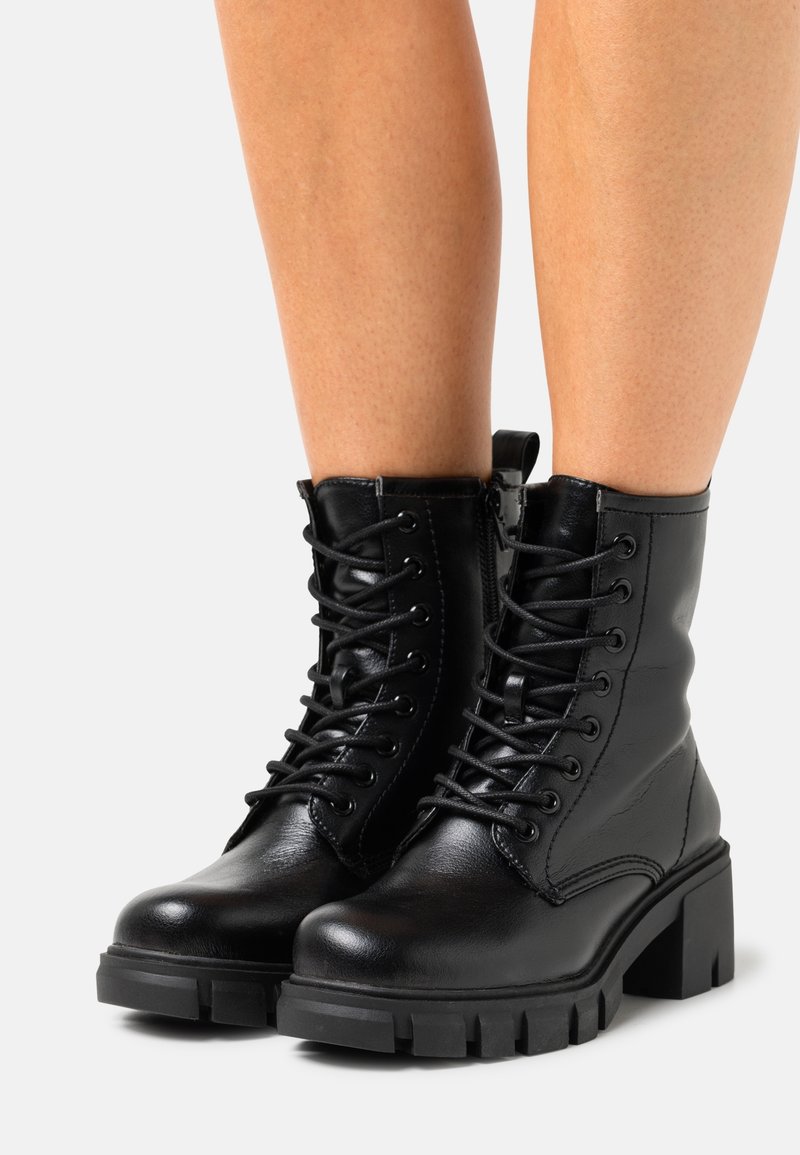Bottes chevilles en cuir noir avec un design à lacets, talon bloc et semelle robuste. La surface est lisse avec des détails de couture et une languette de tirage.