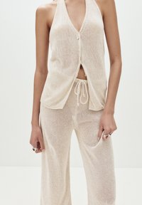 Ljusbeige stickad tvådelad outfit som består av en ärmlös topp med knappar och lösa byxor med dragband och fickor.