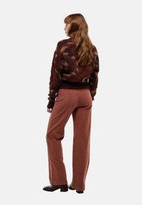 Pull en tricot avec un motif multicolore, ourlet côtelé brun foncé ; associé à un pantalon en velours côtelé terracotta à jambes larges et des bottes à talons noires.