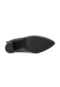 Chaussure noire à talons hauts avec un bout pointu, comportant un dessus en textile texturé et une semelle en caoutchouc avec un détail d'emblème circulaire.