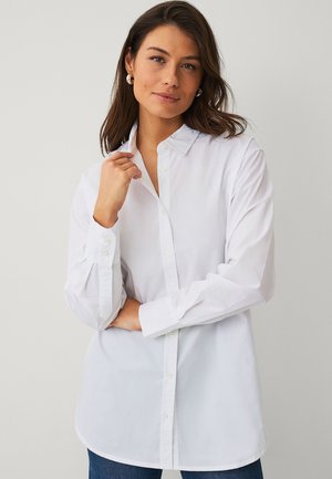 Witte blouse met lange mouwen en knoopsluiting, met een gestructureerde kraag, manchetten met knopen en een losse pasvorm, gecombineerd met een blauwe jeans.