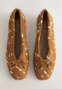 Paire de ballerines marron avec des taches blanches, surface texturée semblable à de la fourrure et petits nœuds sur le devant, placées côte à côte.