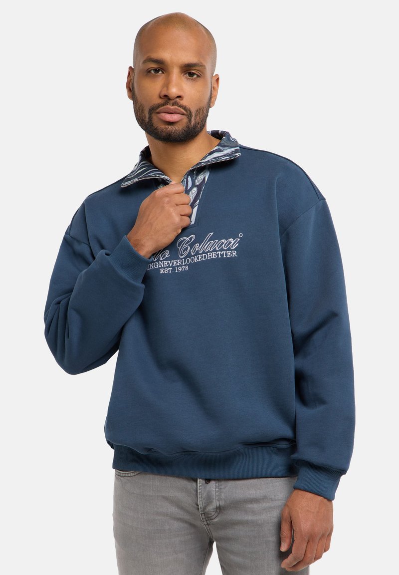 Navy blue pullover sweatshirt with a half-zip collar, featuring patterned lining, ribbed cuffs, and embroidered text on the front.