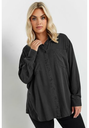 Overmaatse zwarte button-up shirt gemaakt van een zacht materiaal, met een enkele borstzak en lange mouwen met knoopmanchetten.