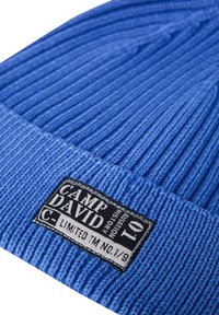 Blue knitted beanie with ribbed texture; black label with white text "CAMP DAVID LIMITED TM NO. 1/9" on the folded edge.