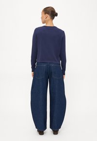 Felpa navy a maniche lunghe e jeans in denim blu scuro con gamba larga. I jeans presentano due tasche posteriori e una vestibilità comoda. Tessuti morbidi e solidi.