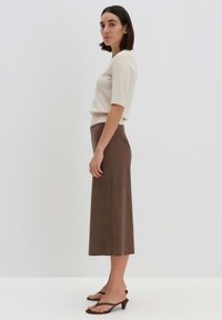 Maglione crema a maniche corte abbinato a una gonna in pelle marrone di lunghezza media. Presenta una texture semplice e liscia e linee pulite.