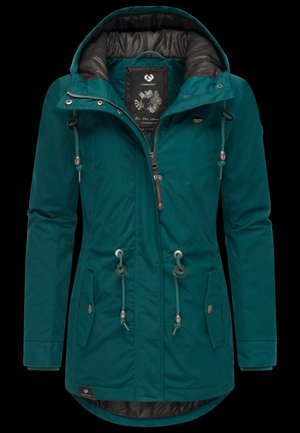 Giacca impermeabile color verde petrolio con cappuccio regolabile tramite coulisse, chiusura frontale con cerniera, due tasche laterali e rivestimento interno a contrasto. Presenta dettagli decorativi in metallo.