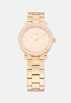 Gold-tone metal watch with a round dial, large numeral markers, and a crystal-accented bezel. Features a linked bracelet strap.