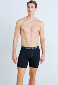 Boxers ajustés pour hommes noirs avec un design ajusté, une taille élastique arborant le logo Nike en blancs et accents jaunes. Texture lisse.