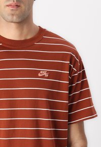 Brunstribet t-shirt med hvide vandrette striber, rund halsudskæring og lille broderet Nike SB-logo på venstre bryst.
