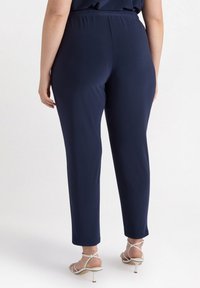 Granatowe spodnie z elastycznym pasem wykonane z gładkiego, rozciągliwego materiału; zwężające się nogawki; noszone z białymi sandałami na obcasie z paskami.
