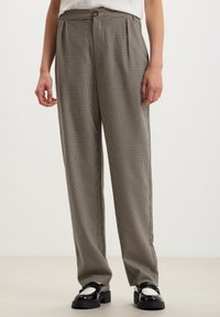 Pantaloni a gamba larga check bianco e nero, con vita alta, pieghe frontali e chiusura con bottone. Indossati con scarpe nere.