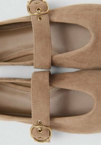 Para beżowych zamszowych balerin Mary Jane z zaokrąglonymi noskami i regulowanymi paskami z złotą sprzączką na górze.