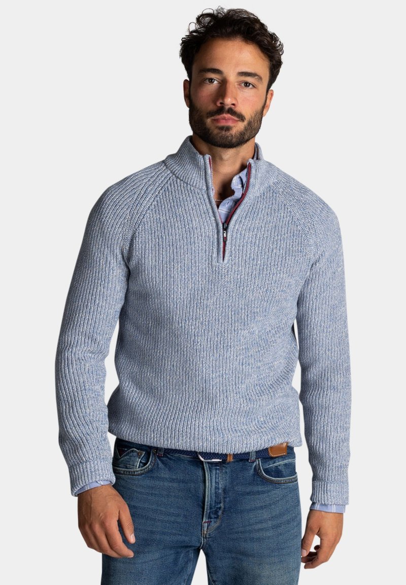 Lichtblauwe gebreide trui met een ritskraag, gegroefde textuur en raglanmouwen, gecombineerd met een overhemd met kraag dat eronder zichtbaar is.
