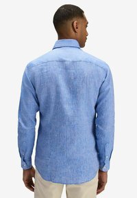 Ljusblå, strukturerad skjorta med knappar, spetsiga kragar, långa ärmar och rundad nederkant. Har ett slitstarkt tyg och vita knappar.