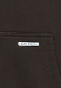 Brauner Stoff mit einer strukturierten Oberfläche und einer Fronttasche. Verfügt über ein rechteckiges silbernes Logoschild mit der Aufschrift "bazix republic".