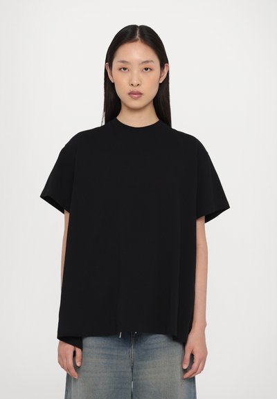 Černé oversized tričko s krátkými rukávy, kulatým výstřihem a měkkou texturou. Spárováno se světle modrými džíny, minimalistický design.