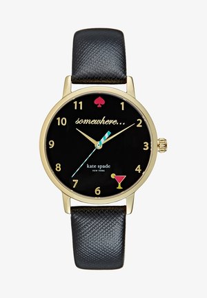 Złoty zegarek Kate Spade z czarnym teksturowanym paskiem, czarną tarczą, złotymi cyframi, paskowaną sekundową wskazówką i ikoną kieliszka do koktajli przy godzinie 5.