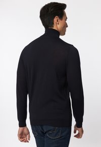 Maglione a collo alto blu navy con colletto e polsini a coste, realizzato in tessuto leggero. Dettagli delle cuciture lungo le spalle, indossato con jeans scuri.