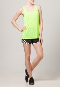 Limonkowo zielony sportowy tank top z poziomymi paskami, w połączeniu z czarnymi szortami z białymi akcentami. Lekka tkanina zapewniająca komfort.