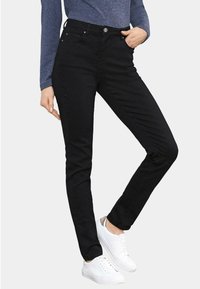 Schwarze Jeans im Slim-Fit mit sichtbaren Vorderfächern, Metallknopfverschluss und minimalistischen Design, kombiniert mit weißen Sneakers.