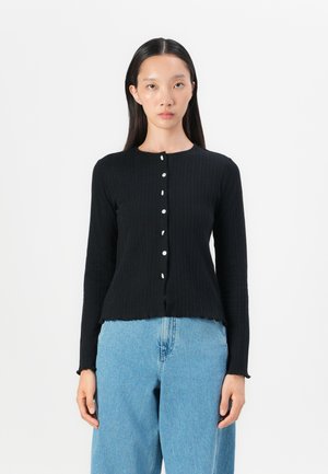 Schwarze gerippte Langarm-Cardigan mit Rundhalsausschnitt, ausgestattet mit sechs weißen Knöpfen vorne und einem taillierten, gewellten Saum.