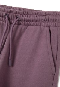 Lila Jogginghosen mit einem Kordelzugbund, weichem Material, seitlichen Taschen und gerippten Bündchen. Glatter Stoff mit minimalen Verzierungen.