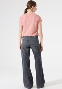 Haut rose clair à manches courtes avec une coupe décontractée, associé à un jean larges taille haute gris foncé avec poches arrière et couture minimale.