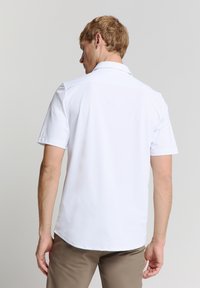 Witte korteblauwe shirt, gladde stof, opgevouwen kraag, vlakke achterkant, zichtbare stiksels en een licht gebogen zoom.
