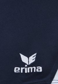 Marineblauwe textuurstof met een wit geborduurd logo met gestileerde vleugels en de tekst "erima." Geen aanvullende patronen of accenten.