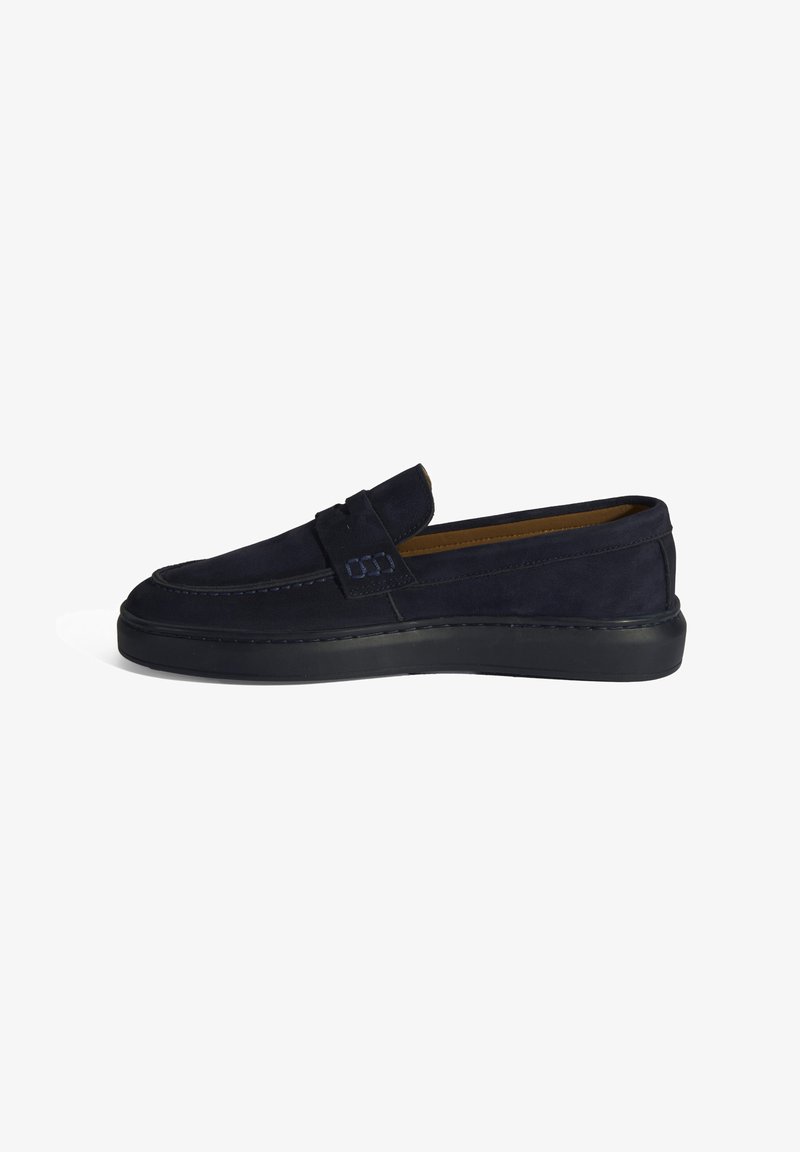 Mocassins en nubuck bleu marine foncé avec une semelle en caoutchouc plate, présentant un design cousu et une sangle asymétrique sur le dessus.