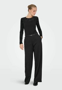 Czarna bluzka z długim rękawem z półprzezroczystym paskiem w paski oraz czarne spodnie z wysokim stanem. Całość dopełniają cienki czarny pasek i botki za kostkę.