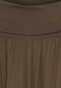 Brun nederdel med en bred elastisk talje. Stoffet er let, tekstureret og har bløde læg for ekstra bevægelse og flow.