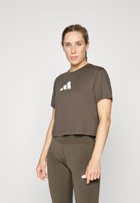 Smeđa skraćena majica s kratkim rukavima i bijelim grafičkim dizajnom. Uparena s odgovarajućim leggingama visokog struka. Glatka, rastezljiva tkanina.