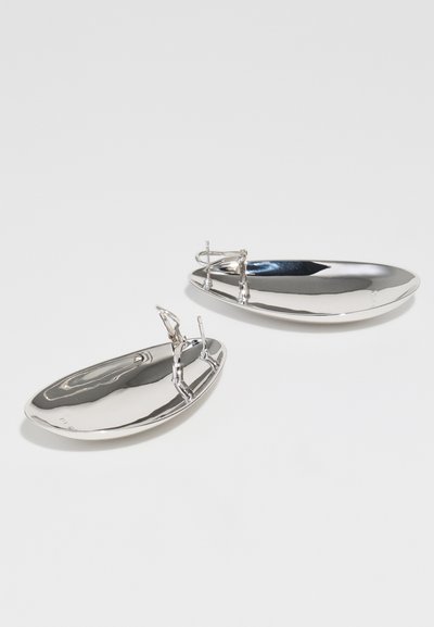 Srebrni kovinski pladnji z sijajno, odbojno površino, ki imajo edinstvene oblikovane figure kot ročaji, v ovalnih oblikah različnih velikosti.